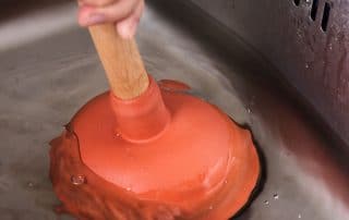 Closeup of person unclogging a sink with a cup plunger