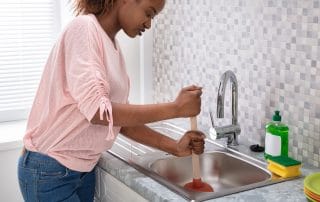 Side View Of A Female Plumber Using Plunger In Kitchen Sink