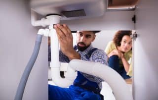 Close up of plumber fixing drain pipe underneath a kitchen sink
