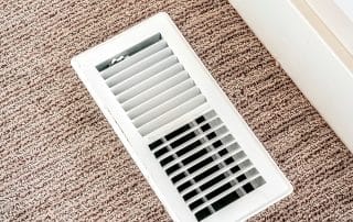 White air conditioner duct grille cover against floor with brown carpet